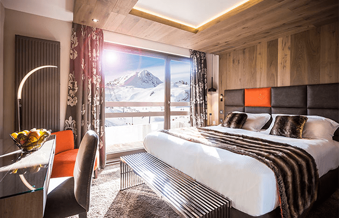 A brown and orange decorated bedroom with a view of the snowy mountains out the window at the luxury hotel Taj-I-Mah